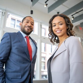 Image of an African American man in a business suit and an African American woman in a business suit smiling at the camera for the blog "Integrating DEI into Your Interviewing and Hiring Process"