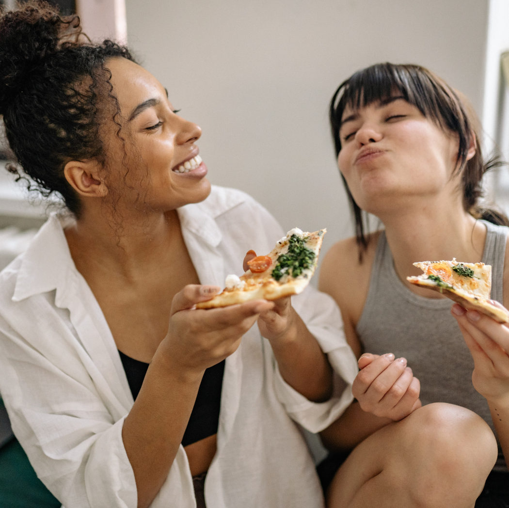 Image of two diverse women enjoying slices of pizza for the blog "LGBTQ Job Applicants May Want to Mention Their Sexual Orientation or Identity During the Interview. Are Your Hiring Managers and Interviewers Prepared?"
